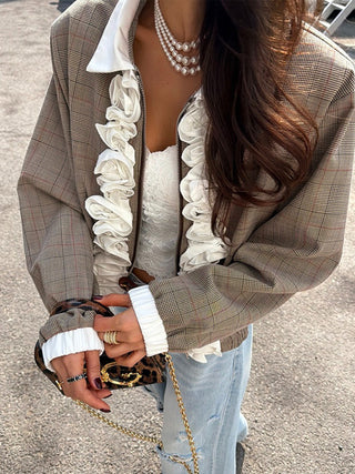 Model wearing a cropped plaid jacket with white ruffle trim over a lace top and jeans