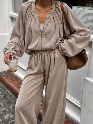 Model wearing a black satin-look zip jacket and matching wide-leg pants