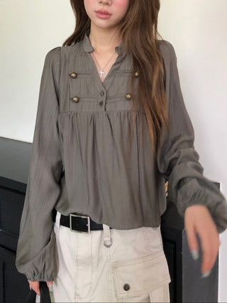 Model wearing an ivory white long-sleeve pleated blouse with front pockets and rounded button accents