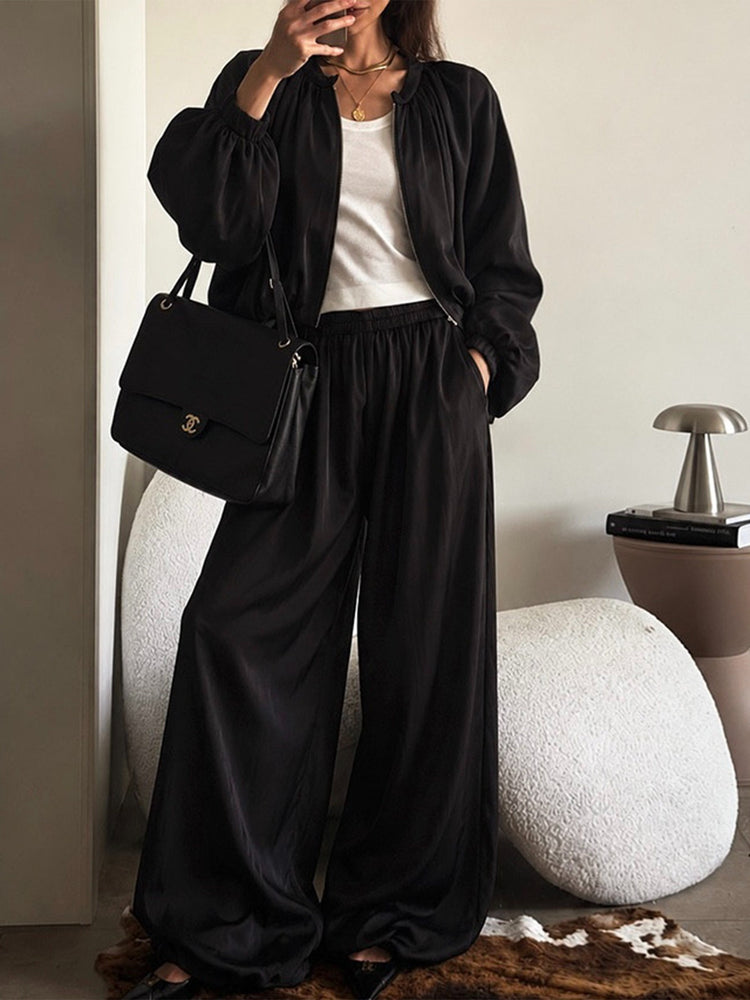 Seated model wearing a black relaxed jacket and wide-leg pants set